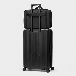 A black hard-shell rolling suitcase with an extended telescoping handle, stacked underneath a matching black soft-sided bag with a top handle, shown on a light gray studio background.
