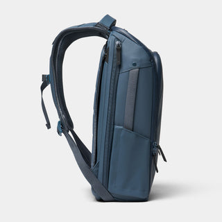 A slate blue backpack shown from a side profile view against a light gray background.