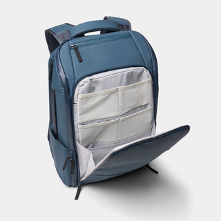 A slate blue backpack shown open to reveal a light gray interior organizer pocket with mesh and zip compartments, photographed on a clean light gray background.