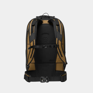 The back view of a technical backpack in black and tan, showing padded shoulder straps, a central compression buckle strap, and a top carry loop on a white background.