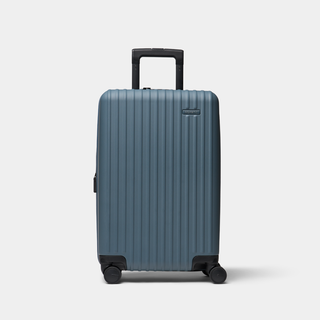 A blue hard-shell carry-on suitcase with vertical grooves, a telescoping handle, and four wheels, shown on a light gray background.