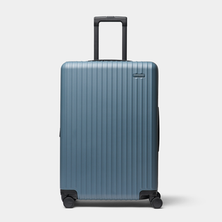 A blue ribbed hard-shell suitcase with an extended black telescoping handle and four spinner wheels, shown on a light gray background.