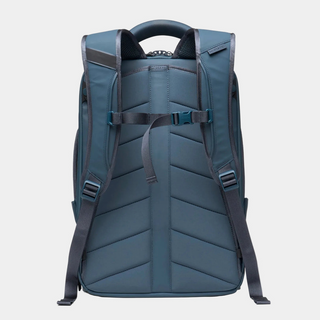 The back view of a dark slate blue backpack with padded shoulder straps, adjustable buckled straps, and a top carry handle, shown on a light gray background.