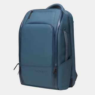 A slate blue Nomatic backpack shown from a three-quarter angle against a light gray background.