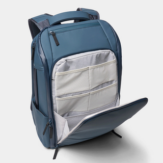 A blue-gray backpack shown open to reveal its light gray interior compartments, photographed on a clean light gray studio background.
