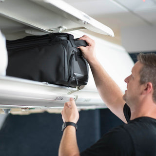 NOMATIC Travel Bag 30L in black, being placed in an airplane overhead bin